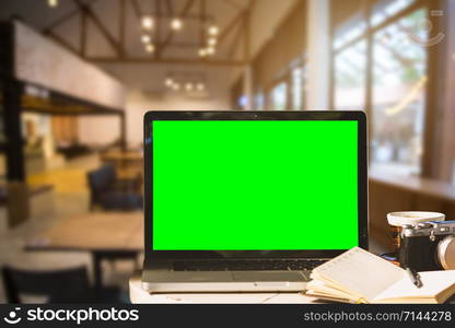 Mockup image of laptop with blank green screen with camera,notebook,coffee cup on wooden table of In the coffee shop background.