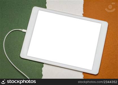 mockup of digital tablet with a blank isolated screen (clipping path included) against paper abstract in colors of Irish national flag,green, white and orange