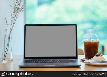Mockup of laptop computer with empty black gray screen of ice coffee in cup mug and Homemade white orange cake on wood desk office desk in coffee shop at the cafe,during business work concept