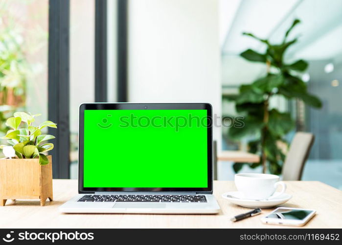 Mockup of laptop computer with empty green screen with coffee cup on table of the coffee shop background