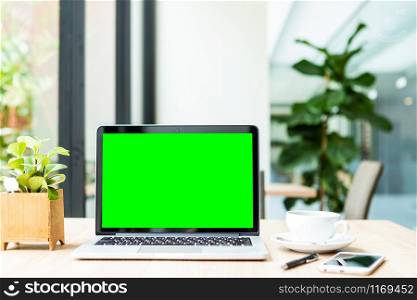 Mockup of laptop computer with empty green screen with coffee cup on table of the coffee shop background