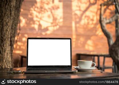 Mockup of laptop computer with empty screen with coffee cup and smartphone on table of tree branch shadow the cafe coffee shop background,White screen