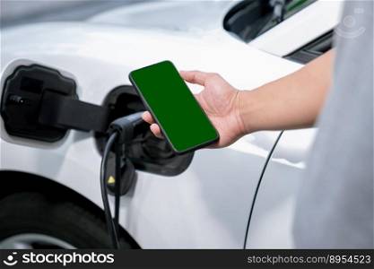 Mockup phone with green screen display energy status of electric vehicle connected to charging station for copyspace. Progressive concept for clean environment. EV powered by green renewable energy.. Progressive concept of green screen mockup phone, EV car and charging station.
