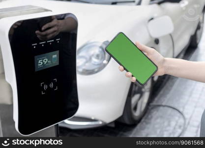 Mockup phone with green screen display energy status of electric vehicle connected to charging station for copyspace. Progressive concept for clean environment. EV powered by green renewable energy.. Progressive concept of green screen mockup phone, EV car and charging station.