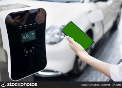 Mockup phone with green screen display energy status of electric vehicle connected to charging station for copyspace. Progressive concept for clean environment. EV powered by green renewable energy.. Progressive concept of green screen mockup phone, EV car and charging station.