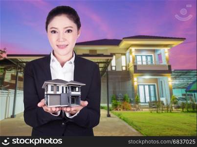 model house in business woman hand with actual house and garden bacground