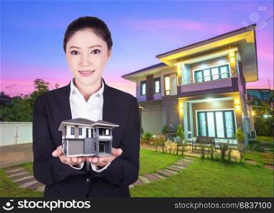 model house in business woman hand with actual house and garden bacground