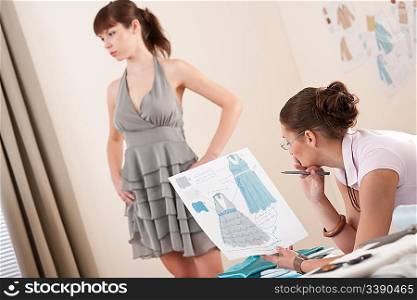 Model in gray dress fitting by female fashion designer studio