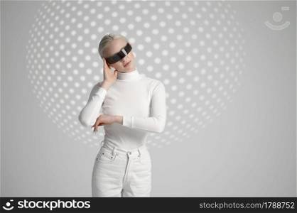 Model in white clothes and futuristic glasses, light grey background. Female person in virtual reality style, future technology, futurism concept. Model in white clothes and futuristic glasses