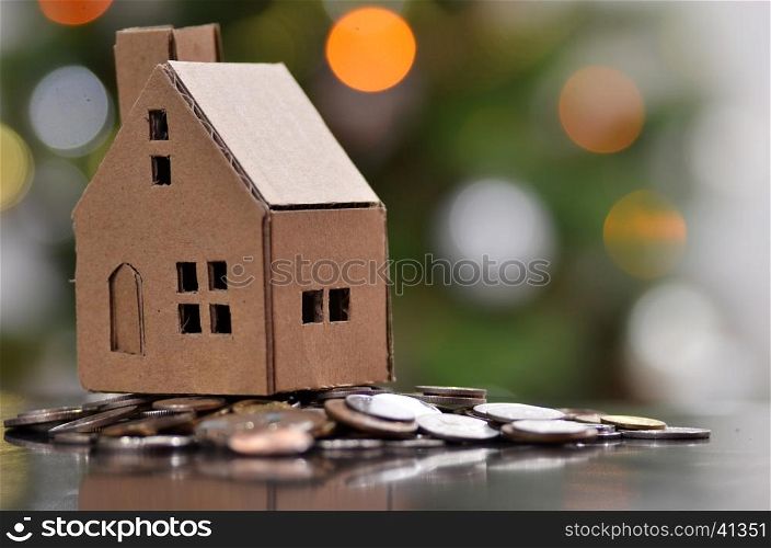 Model of house with coins on wooden table on blurred background