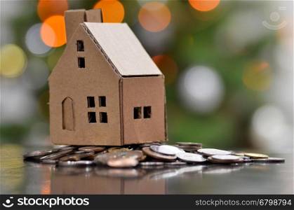 Model of house with coins on wooden table on blurred background