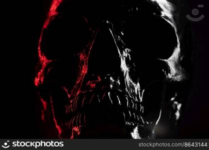 Model of human skull painted with black on dark background with illumination. Concept of fear and horror, Halloween celebration. Copy space.. Model of human skull painted with black on dark background with illumination. Concept of fear and horror, Halloween celebration. Copy space