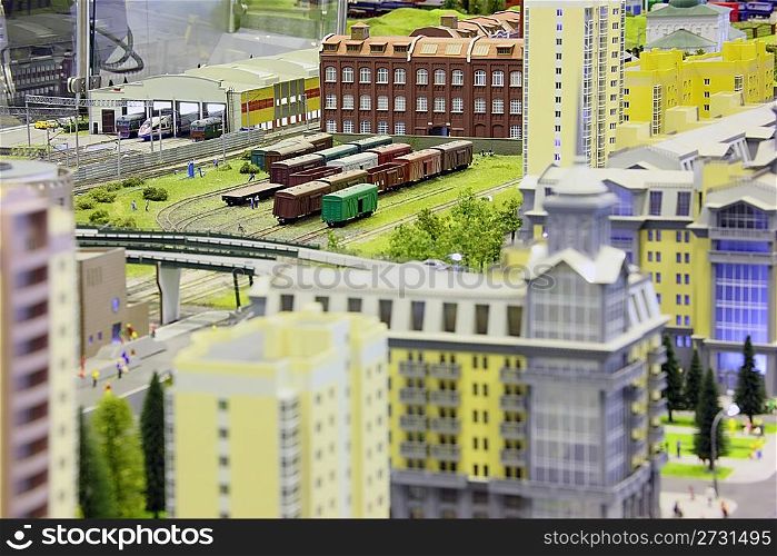 model of railroad station. railroad, trains, buildings and other constructions. focus on three floors building in top of image.