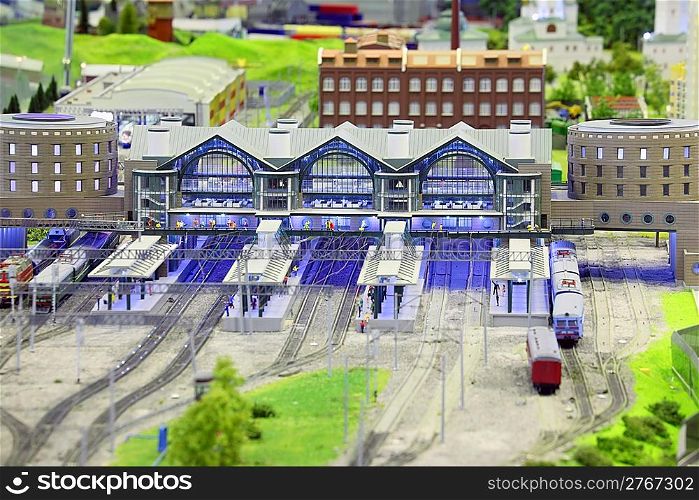 model of railroad station. railroad, trains, trees, grass, humans and buildings. focus on building in center of image.