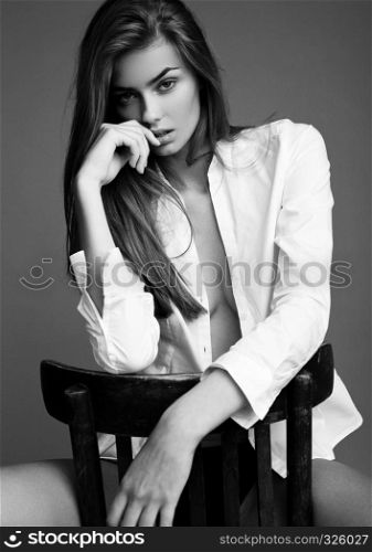 Model test with young beautiful fashion model wearing white shirt sitting on chair on grey background