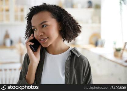 Modern african american girl talking on smartphone at home, stylish young woman with afro hairs answer mobile phone call, having conversation with friends or relatives indoors.. Modern african american young girl talking on smartphone, answering mobile phone call at home