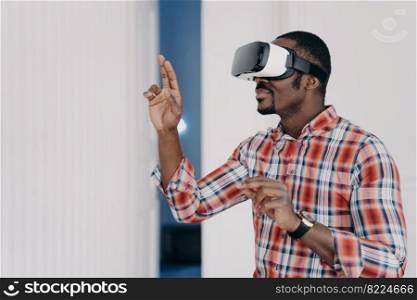 Modern african american guy wearing virtual reality glasses, touching virtual objects by fingers, interacts with cyberspace. Black man gamer in VR goggles playing video game. High tech, entertainment.. African american guy in vr glasses interacts with virtual augmented reality, playing video game