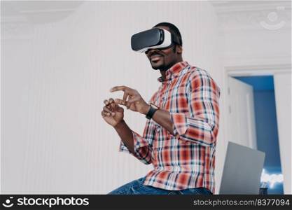 Modern african american man in VR glasses enjoy virtual tour in augmented cyberspace, touch 3d objects, interacting with digital interface. Black guy uses virtual reality goggles for online shopping.. Modern african american man in virtual reality glasses enjoying virtual tour in augmented cyberspace