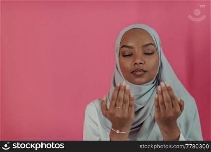 Modern African Muslim woman makes traditional prayer to God, keeps hands in praying gesture, wears traditional white clothes, has serious facial expression, isolated over plastic pink background. High-quality photo. Modern African Muslim woman makes traditional prayer to God, keeps hands in praying gesture, wears traditional white clothes, has serious facial expression, isolated over plastic pink background