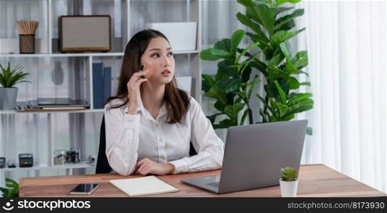 Modern and young enthusiastic businesswoman multitasks by checking her smartphone for business matters and working with laptop in her desk at the office.. Young enthusiastic businesswoman using smartphone and laptop in office.