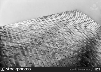 Modern architectural abstract of a section of a wall made of many metal panels reflecting light that stretches towards the sky.