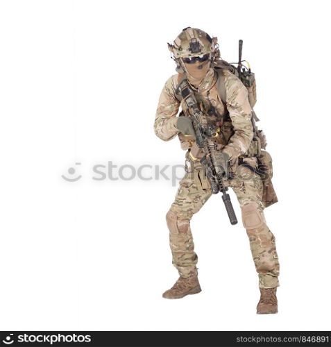 Modern army infantry rifleman in camo uniform, radio headset on helmet, ammo on load carrier, sneaking, crouching, aiming and shooting with service rifle studio shoot isolated on white background. Army soldier crouching with rifle studio shoot
