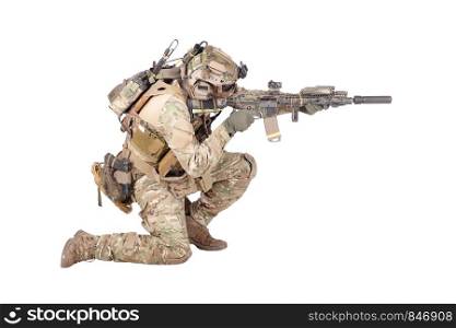 Modern army infantry soldier in combat uniform and helmet standing on knee, aiming with laser sight on service rifle, shooting in enemy during firefight studio shoot isolated on white background. Soldier shooting from knee isolated studio shoot