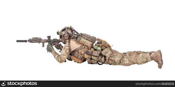 Modern army soldier, infantry rifleman equipped with tactical ammunition and radio, lying on ground, observing territory trough optical sight, aiming, shooting with assault rifle isolated studio shoot. Soldier shooting from ground isolated studio shoot