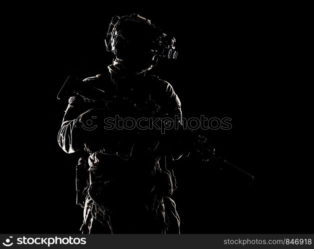 Modern army special operations forces soldier, elite troops rifleman standing in darkness with service rifle, wearing night vision device on battle helmet, low key studio portrait on black background. Special forces fighter in darkness studio shoot