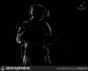 Modern army special operations forces soldier, elite troops rifleman standing in darkness with service rifle, wearing night vision device on battle helmet, low key studio portrait on black background. Special forces fighter in darkness studio shoot