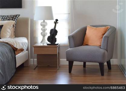 modern bedroom interior with orange pillow on grey chair and bedside table lamp at home