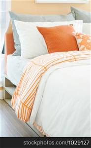 Modern bedroom interior with roll of orange, white and gray pillows on bed