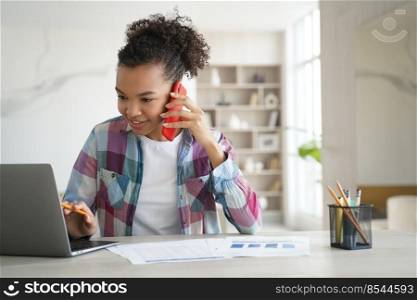 Modern biracial teen girl student discuss learning task with classmate by phone call looking at laptop. Teenager schoolgirl talking with friend while doing homework sitting at desk at home.. Biracial teen girl student discuss homework with classmate by phone call looking at laptop at home