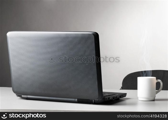 modern black laptop with white cup of coffee with steam