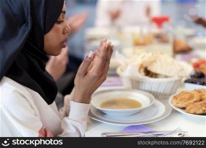 modern black muslim woman praying before having iftar dinner together with multiethnic family during a ramadan feast at home