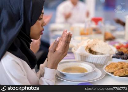 modern black muslim woman praying before having iftar dinner together with multiethnic family during a ramadan feast at home