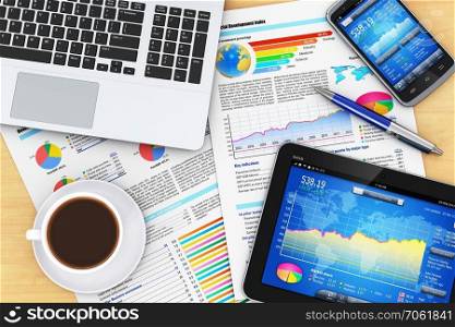 Modern business office workplace technology concept: laptop computer, tablet PC, black glossy touchscreen smartphone with stock market financial application, documents with financial reports, graphs and charts, ballpoint pen and cup of coffee on wooden office table