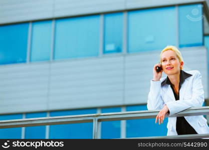 Modern business woman leaning on railing at office building and talking mobile&#xA;