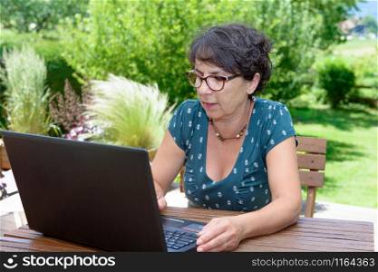 Modern casual woman sitting at garden with a laptop
