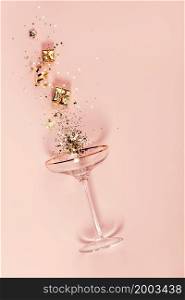 Modern champagne glass with splash of confetti and decorations over pink background. Overhead view, Christmas and New Year concept