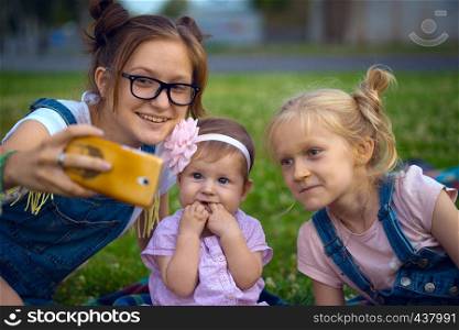 Modern children - girls do selfie sitting on the lawn