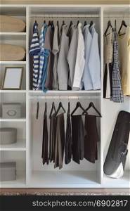 modern closet with row of cloths hanging in white wardrobe