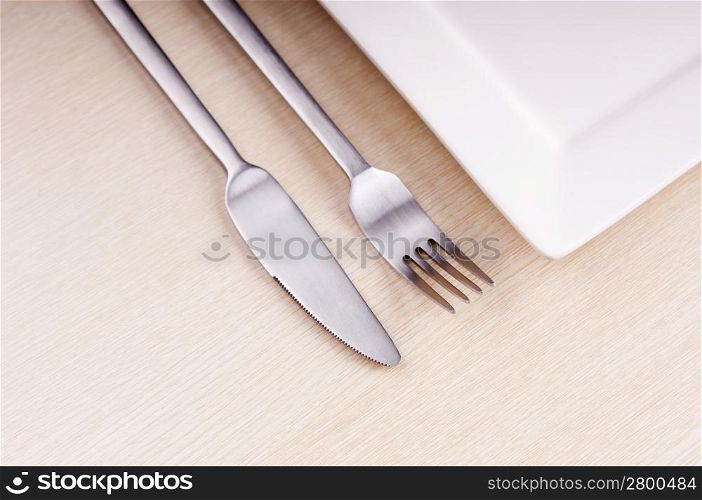 Modern composition of knife, fork and white plate on wooden table