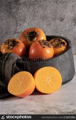 Modern design black ceramic bowl with persimmon fruits on countertop and background.