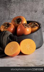 Modern design black ceramic bowl with persimmon fruits on countertop and background.