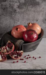 Modern design black ceramic bowl with pomegranate fruit on dark countertop and background.