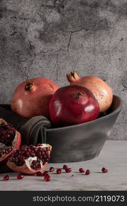 Modern design black ceramic bowl with pomegranate fruit on dark countertop and background.