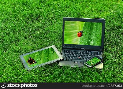 Modern digital tablet PC with mobile smartphone and laptop on green grass