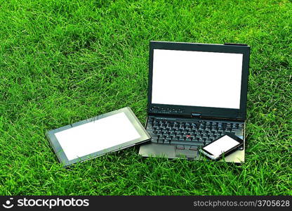 Modern digital tablet PC with mobile smartphone and laptop on green grass