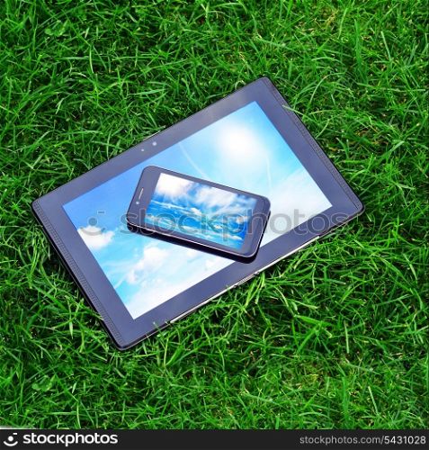 Modern digital tablet PC with mobile smartphone on green grass